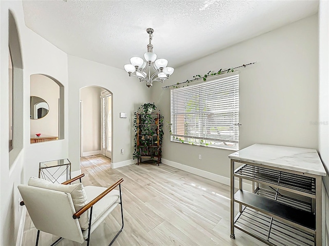sitting room featuring arched walkways, a textured ceiling, a chandelier, and light wood-type flooring