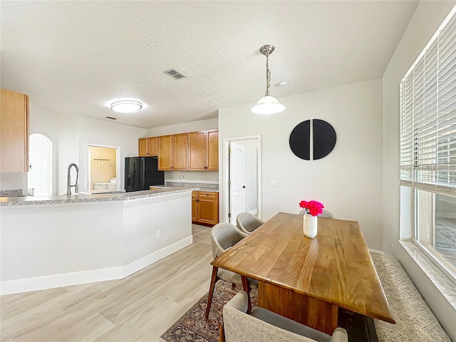 dining area with visible vents, baseboards, light wood-type flooring, a textured ceiling, and arched walkways