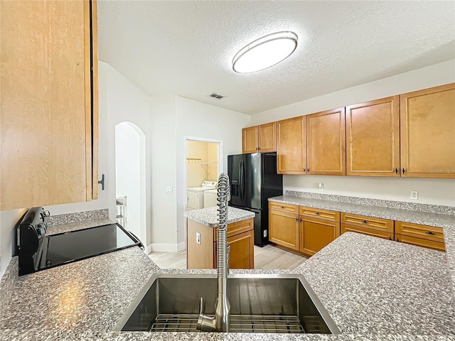 kitchen featuring visible vents, a textured ceiling, separate washer and dryer, arched walkways, and black appliances