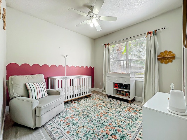 bedroom featuring baseboards, ceiling fan, wood finished floors, and a nursery area