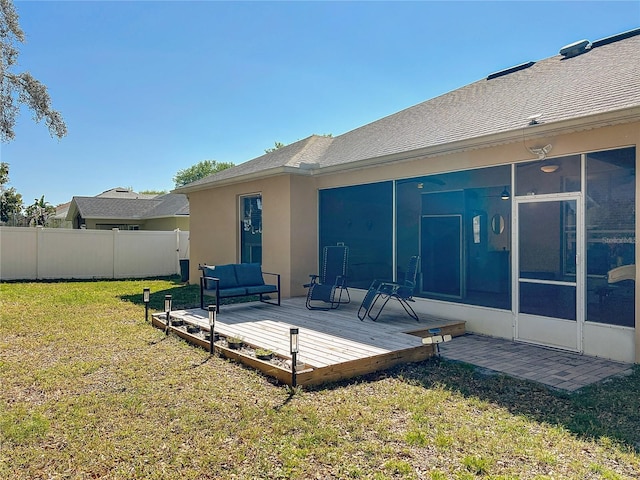 rear view of house featuring fence, a wooden deck, stucco siding, a sunroom, and a yard