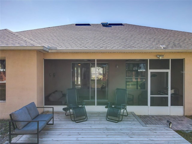 rear view of house featuring roof with shingles, a wooden deck, stucco siding, and an outdoor living space