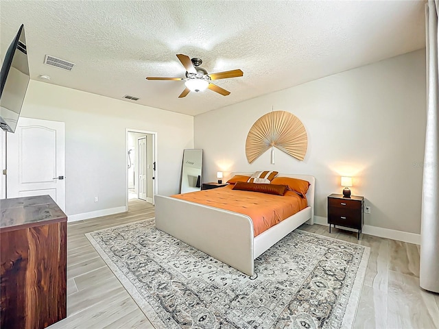 bedroom with baseboards, a textured ceiling, visible vents, and wood finished floors