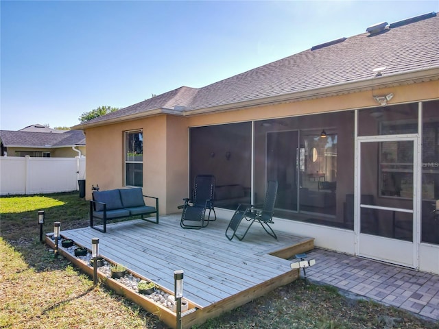 rear view of property with fence, stucco siding, a sunroom, and a deck