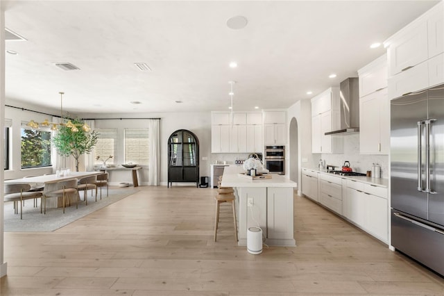 kitchen featuring visible vents, light countertops, decorative backsplash, stainless steel appliances, and wall chimney exhaust hood