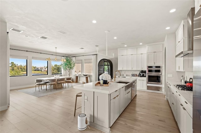 kitchen with visible vents, a sink, light wood-style floors, appliances with stainless steel finishes, and decorative backsplash