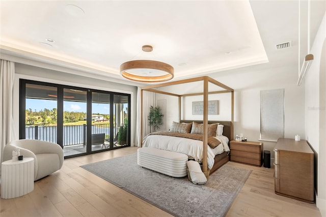 bedroom with access to exterior, visible vents, light wood-style flooring, and a raised ceiling