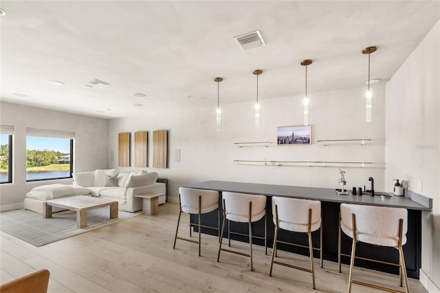 bar featuring light wood finished floors, visible vents, pendant lighting, and indoor wet bar