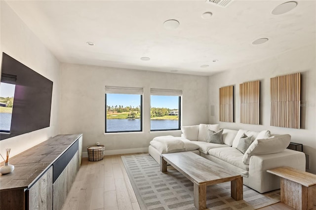 living area with recessed lighting, light wood-type flooring, baseboards, and a water view