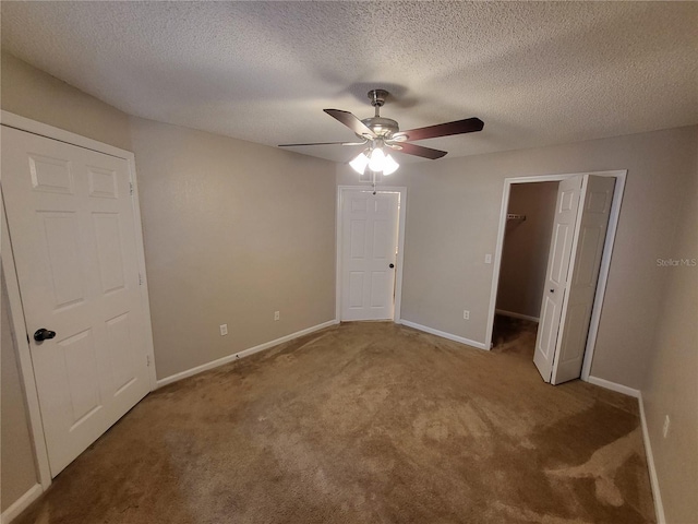 unfurnished bedroom with carpet, baseboards, a ceiling fan, a textured ceiling, and a walk in closet