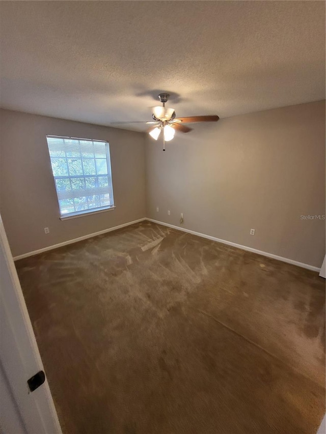 empty room featuring baseboards, a textured ceiling, a ceiling fan, and dark colored carpet