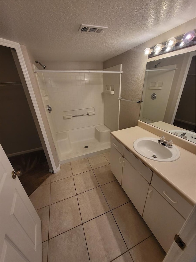 bathroom featuring tile patterned flooring, visible vents, a stall shower, a textured wall, and a textured ceiling