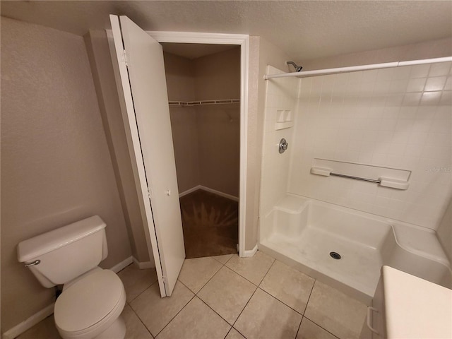 bathroom with toilet, a textured ceiling, a shower stall, tile patterned flooring, and a spacious closet