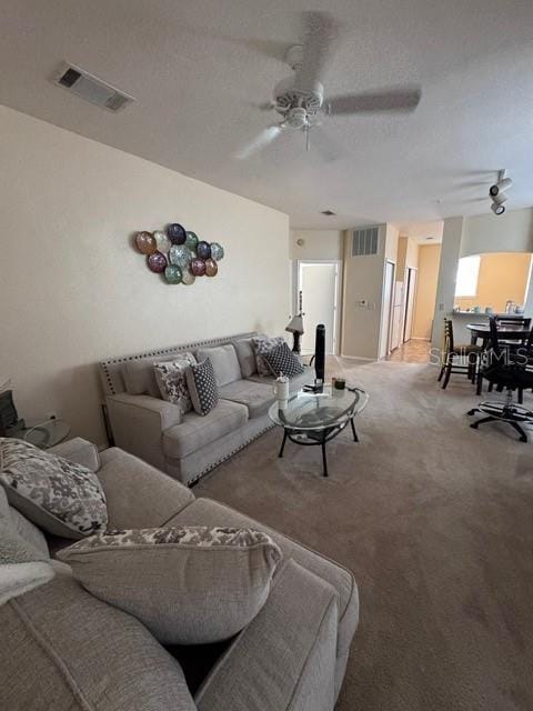 living room featuring visible vents, carpet, ceiling fan, and a textured ceiling