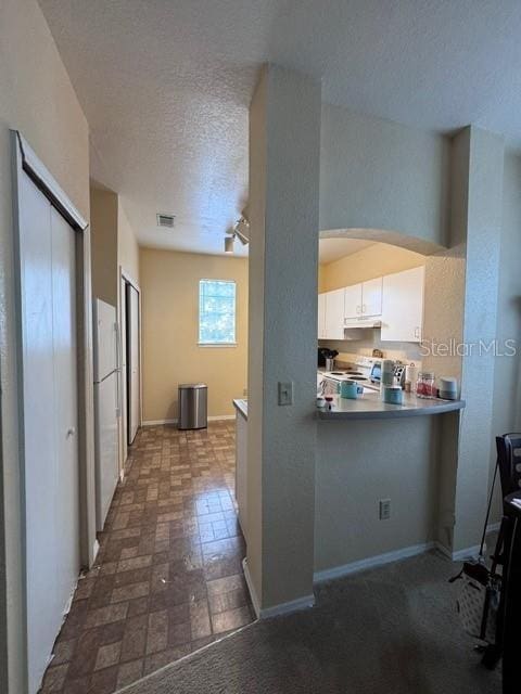 kitchen featuring a textured ceiling, baseboards, arched walkways, range with electric stovetop, and white cabinetry