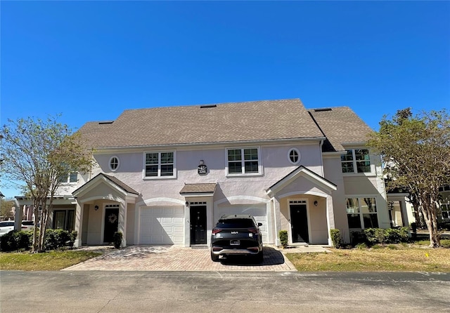 view of front of home with decorative driveway, a shingled roof, an attached garage, and stucco siding