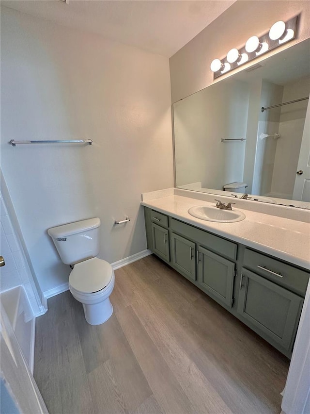 bathroom featuring toilet, wood finished floors, baseboards, walk in shower, and vanity