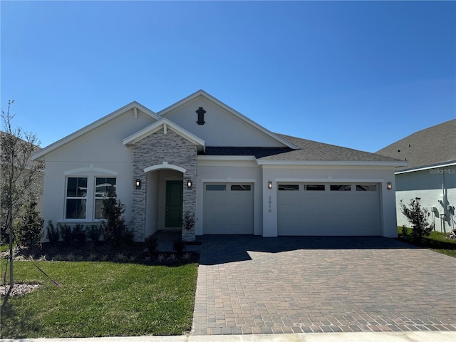 ranch-style house with a front yard, roof with shingles, stucco siding, decorative driveway, and an attached garage