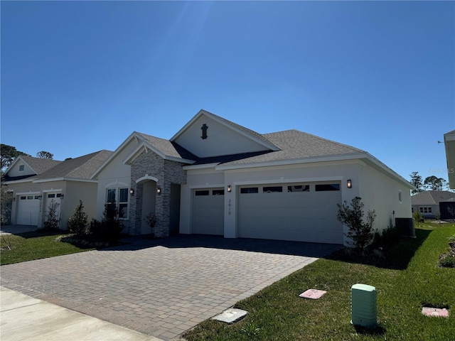 view of front of home with stucco siding, a front lawn, decorative driveway, stone siding, and an attached garage