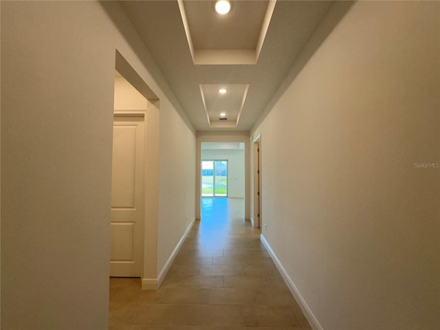 hall with recessed lighting, a tray ceiling, and baseboards