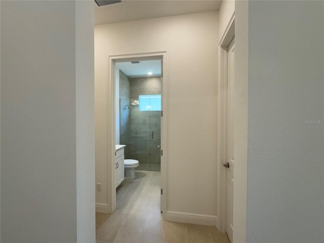 hallway with light tile patterned floors, visible vents, and baseboards