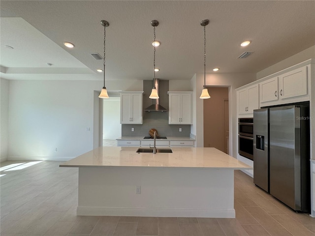 kitchen with visible vents, a sink, stainless steel appliances, wall chimney range hood, and decorative backsplash