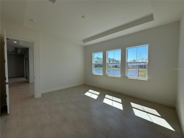 spare room featuring a tray ceiling and baseboards