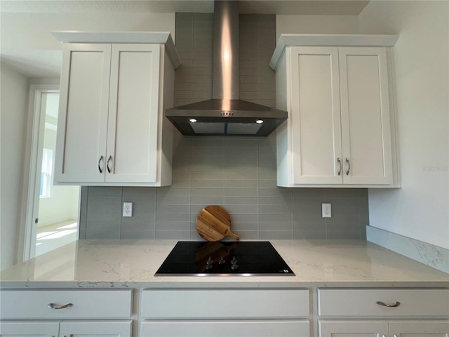 kitchen with black electric stovetop, backsplash, white cabinets, and wall chimney range hood