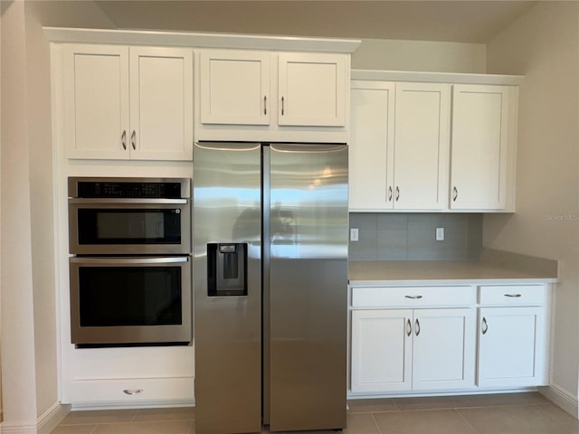 kitchen featuring light tile patterned floors, light countertops, appliances with stainless steel finishes, white cabinetry, and backsplash