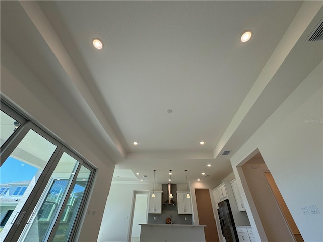 kitchen featuring a tray ceiling, recessed lighting, white cabinetry, wall chimney exhaust hood, and refrigerator with ice dispenser