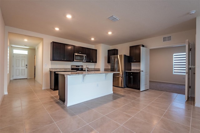 kitchen with visible vents, light stone countertops, a center island with sink, light tile patterned floors, and stainless steel appliances