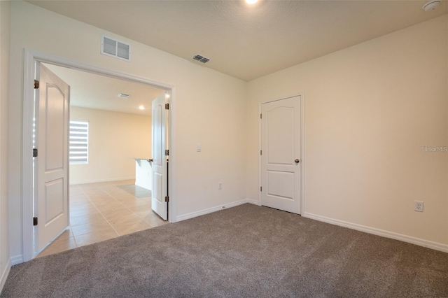 unfurnished room with light carpet, visible vents, baseboards, and light tile patterned floors