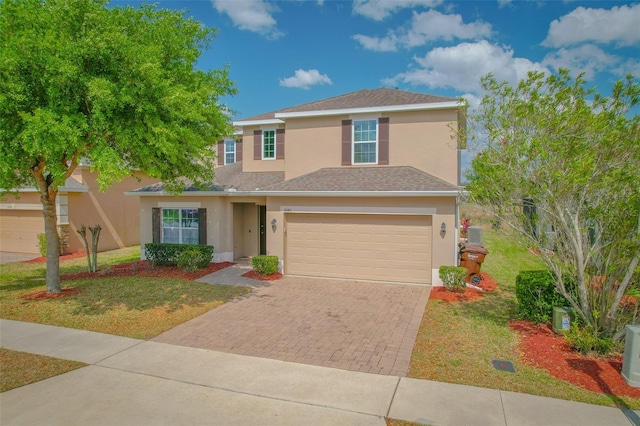 traditional home with a front yard, decorative driveway, a garage, and stucco siding