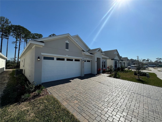 view of front facade featuring stucco siding, central AC, decorative driveway, and a garage