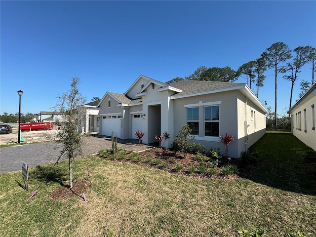 view of front of house with driveway, a shingled roof, stucco siding, a front lawn, and a garage