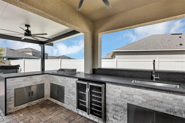 view of patio with beverage cooler, a fenced backyard, an outdoor kitchen, a ceiling fan, and a sink