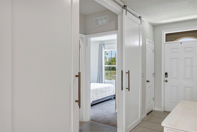 foyer featuring a textured ceiling, light tile patterned floors, visible vents, light carpet, and a barn door