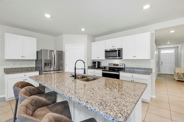 kitchen featuring a sink, stainless steel appliances, a breakfast bar area, light tile patterned flooring, and light stone countertops