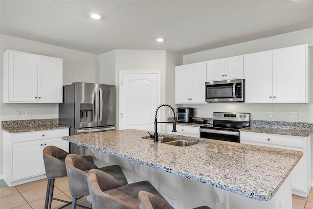 kitchen featuring light stone counters, appliances with stainless steel finishes, a kitchen breakfast bar, light tile patterned flooring, and a sink