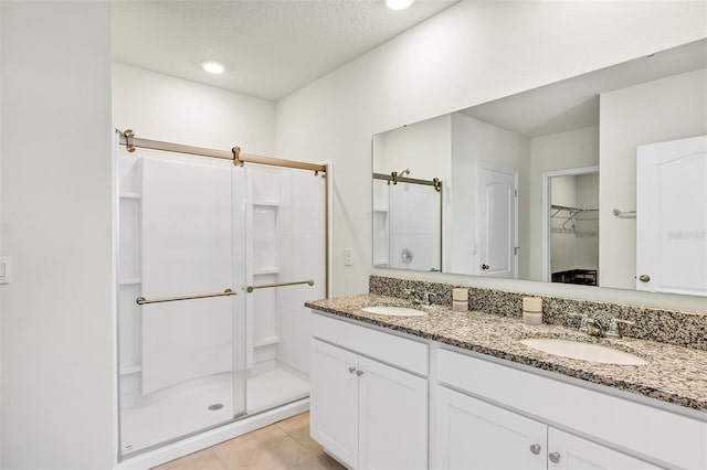 full bath with tile patterned floors, a stall shower, a textured ceiling, and a sink