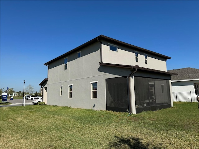 rear view of property with a yard, fence, stucco siding, and a sunroom