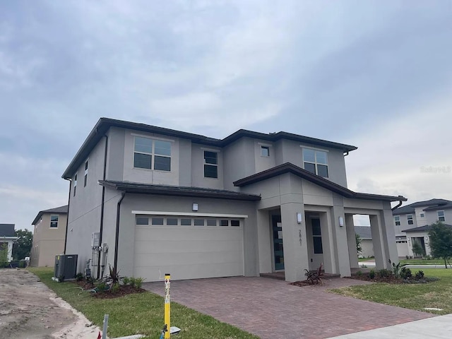 prairie-style home featuring central air condition unit, decorative driveway, an attached garage, and stucco siding