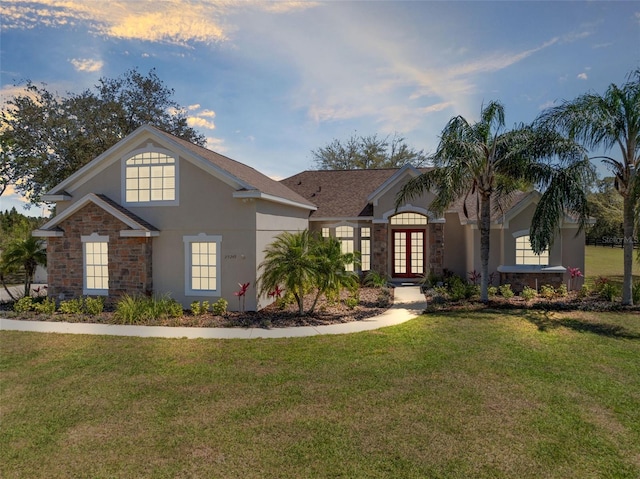 view of front facade featuring a lawn, stone siding, french doors, and stucco siding