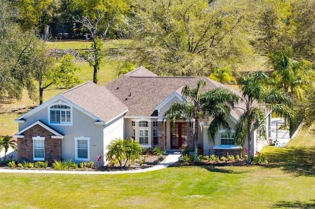 view of front of property featuring a front yard, stone siding, roof with shingles, and stucco siding