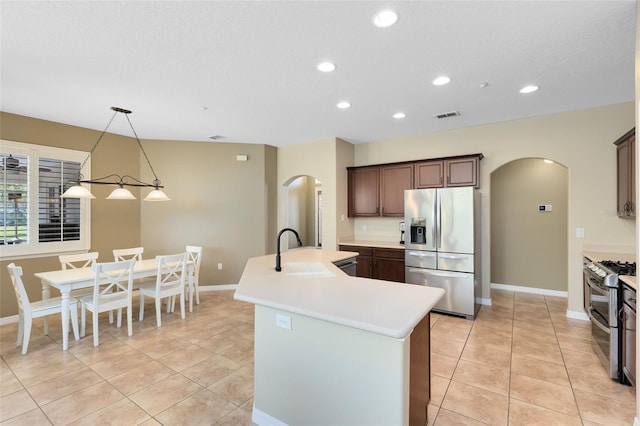 kitchen featuring visible vents, a kitchen island with sink, a sink, arched walkways, and appliances with stainless steel finishes