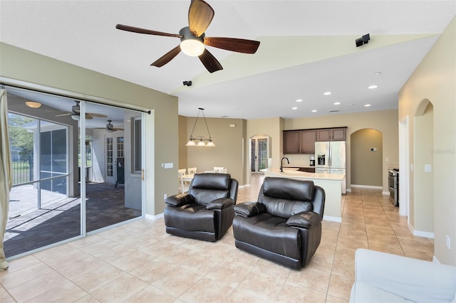 living room with arched walkways, light tile patterned floors, baseboards, ceiling fan, and vaulted ceiling