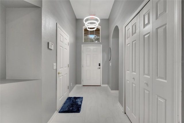 doorway to outside with arched walkways, an inviting chandelier, and baseboards