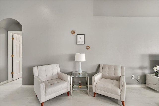 sitting room featuring arched walkways, baseboards, and marble finish floor