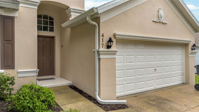 property entrance with stucco siding, an attached garage, and concrete driveway