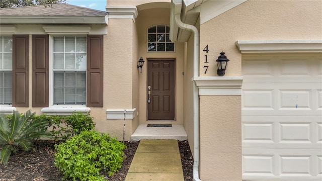 view of exterior entry featuring stucco siding, roof with shingles, and an attached garage